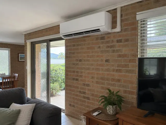 Split system mounted high on a brick wall in a living room with sliding glass doors in Tweed Heads