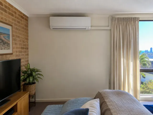 Wall-mounted split system above a living room window with curtains and brick feature wall in Coolangatta